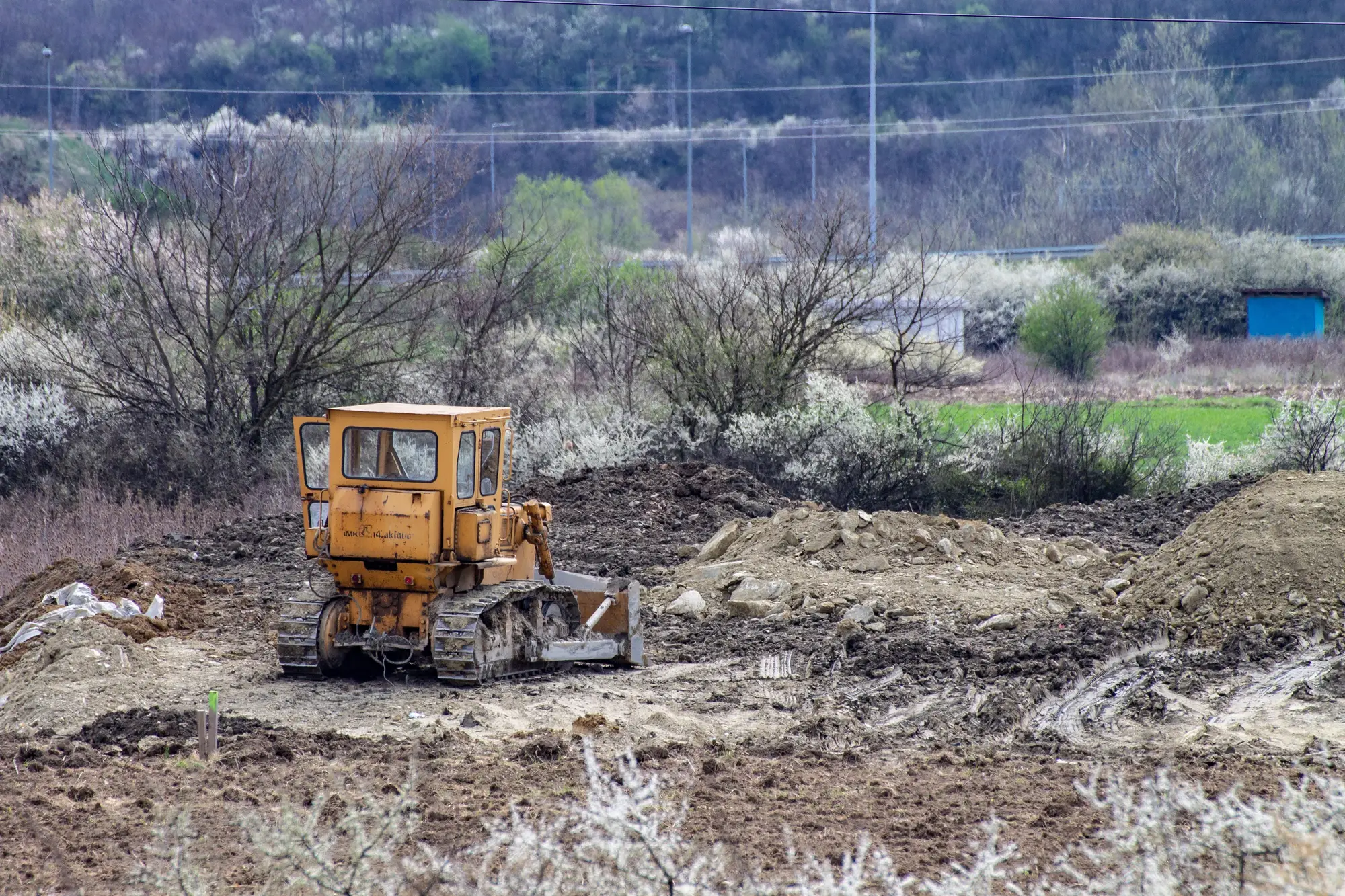 A bulldozer on stripped ground beside spoil piles at the edge of a field