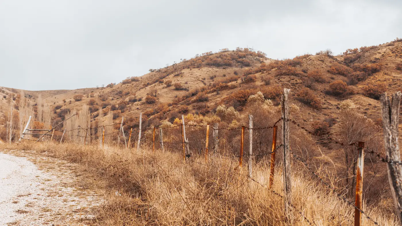 An old barbed wire fence running along dry, scrubby hills under a cloudy sky.
