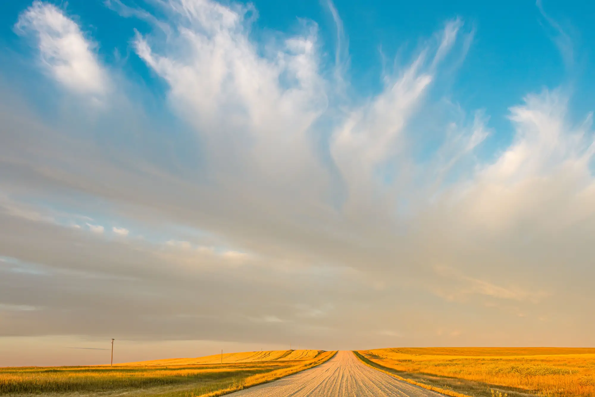 A straight gravel road running across open prairie to the horizon